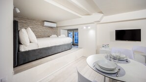Quarto de hotel moderno com cama, área de jantar com mesa posta para dois e televisão na parede.