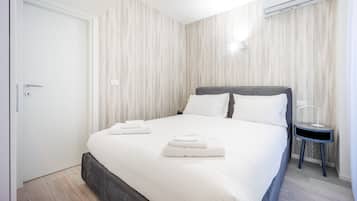 A neatly made bed with two pillows and two folded towels, a bedside table with a lamp, and a door with a keyhole.