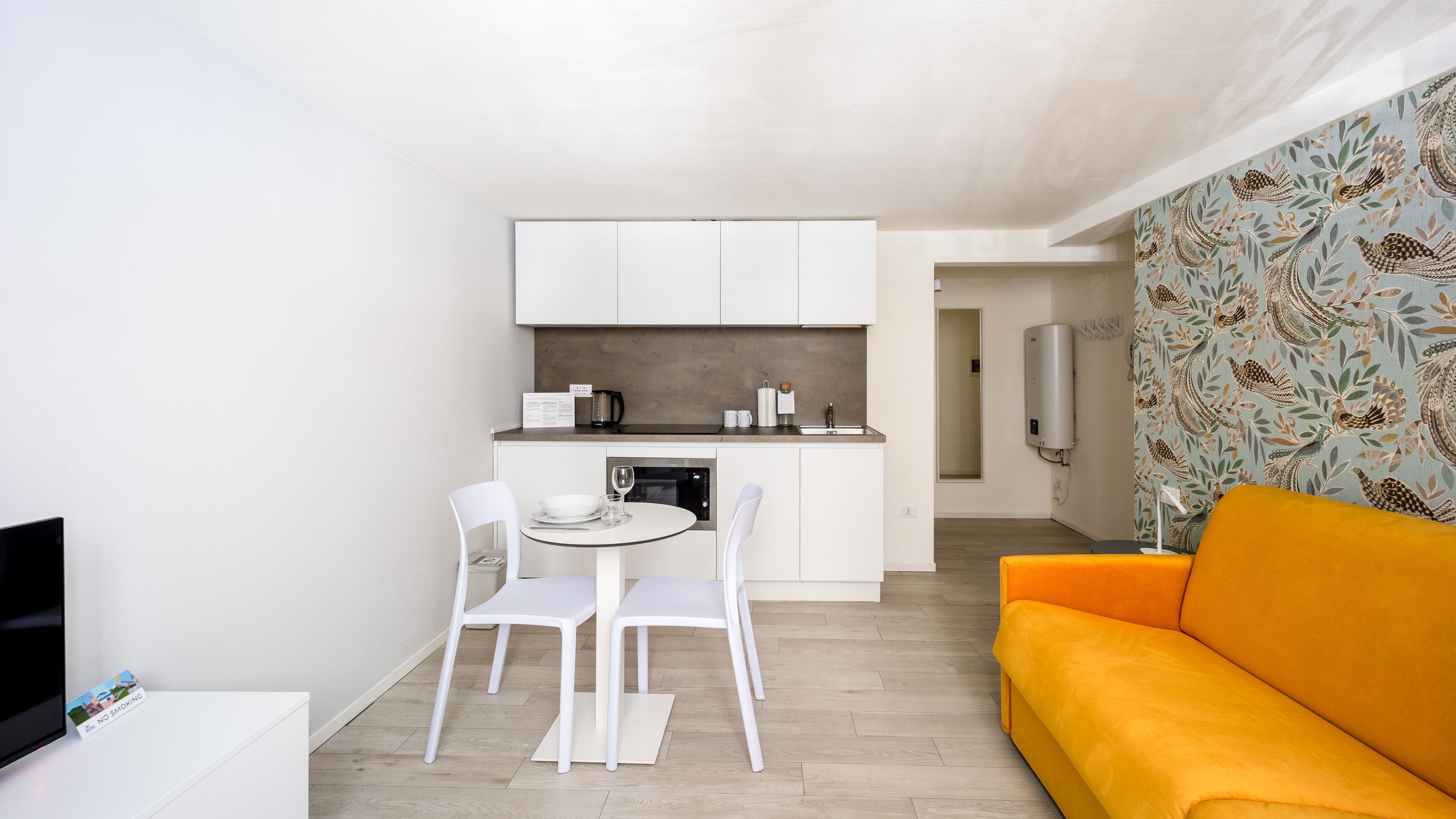 Un espacio habitable compacto con kitchenette, una zona de comedor con dos sillas, un sofá y una pared con diseño.