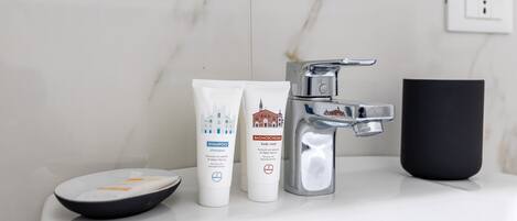 Un lavabo de salle de bain avec un mur en marbre, une tasse noire et deux flacons de produits de toilette.