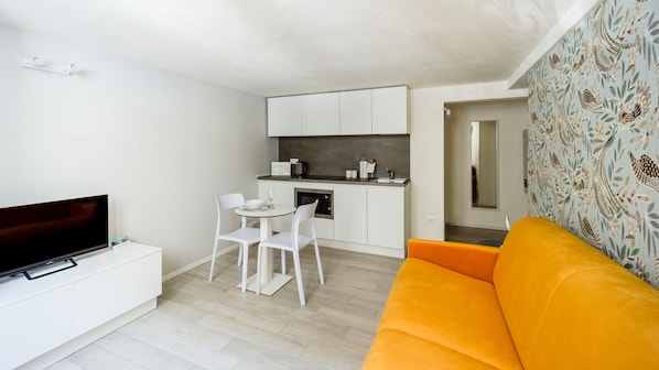 A compact living space with a kitchenette, a dining area with a table and chairs, a sofa, and a flat-screen TV. - Italianway - The B Village Standard (Milan)