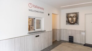Uma área de recepção com um aviso de 'Welcome Point', uma janela com kit de primeiros socorros, uma obra de arte na parede e um balcão de atendimento.