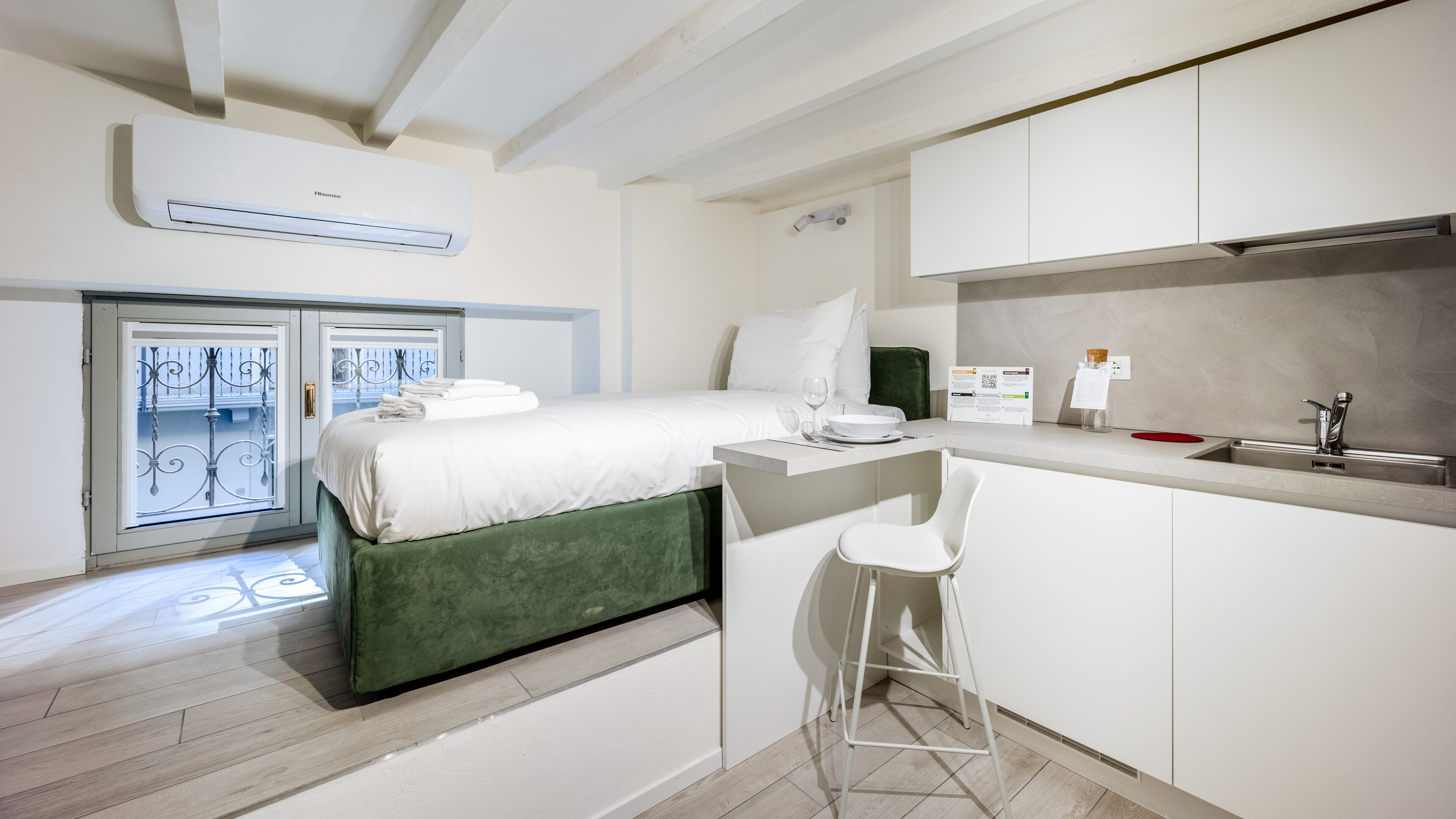 Ein modernes Hotelzimmer mit Bett, einer kleinen Küchenzeile, einer Bar und einem Balkon mit Glastür.