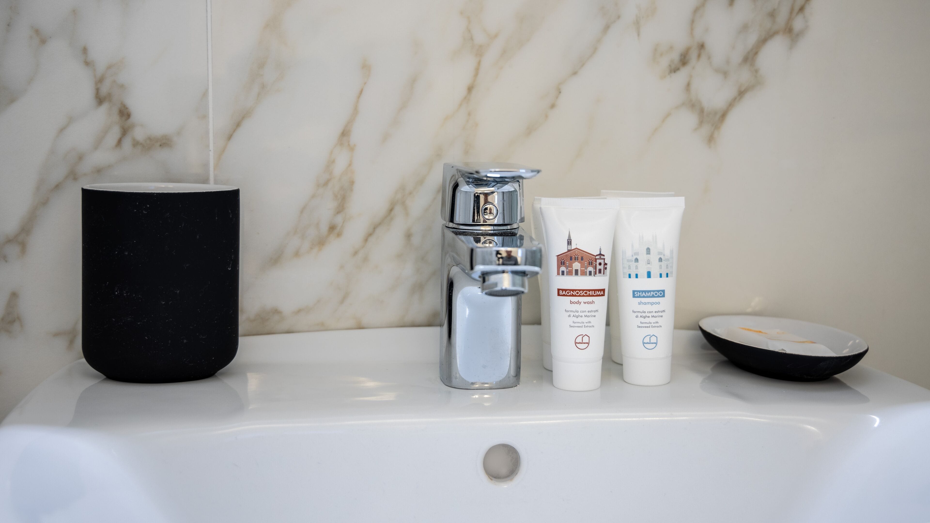 A bathroom sink with a black mug, a silver faucet, and two white bottles of shampoo and body wash.
