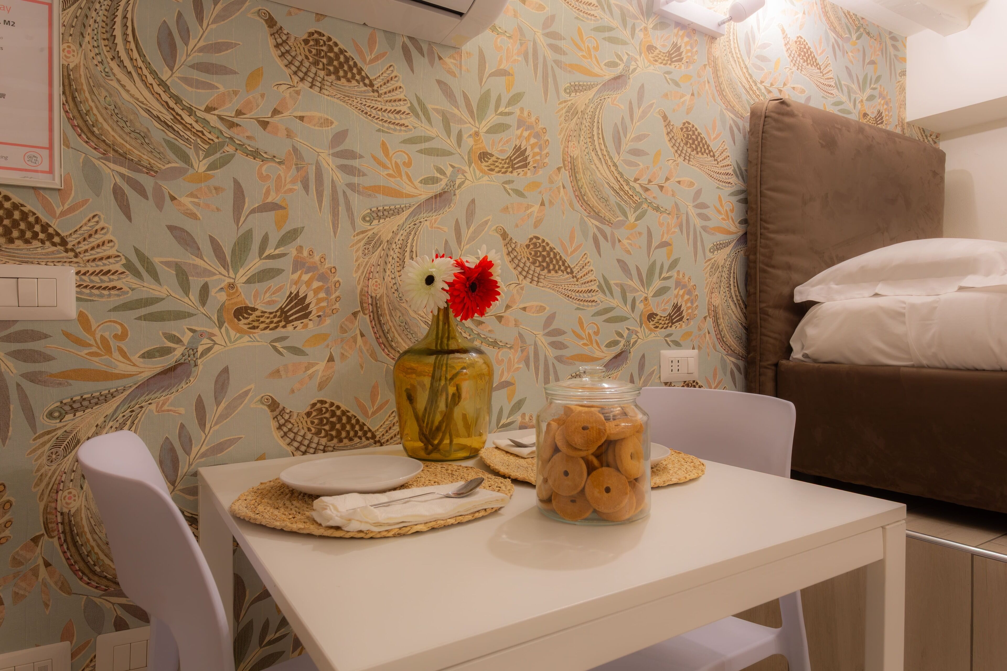 Ein kleiner Essbereich mit Tisch, Stühlen, einer Blumenvase und einer Keksdose.