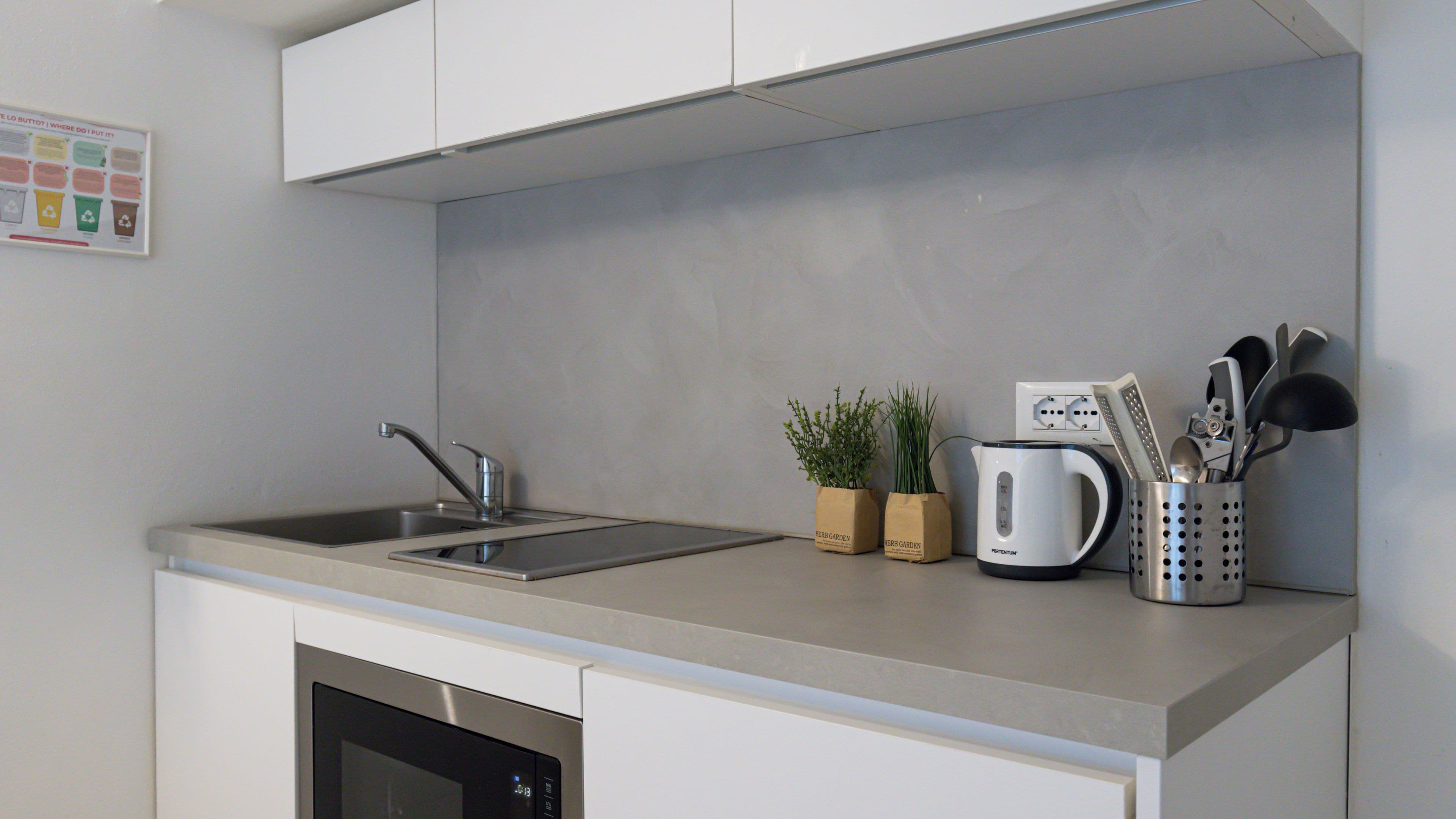 A modern kitchen with a stainless steel sink, a kettle, and a utensil holder.