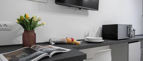 Ett modernt kök med en platt-TV, en mikrovågsugn, en vas med blommor och en tidning på bänkskivan.