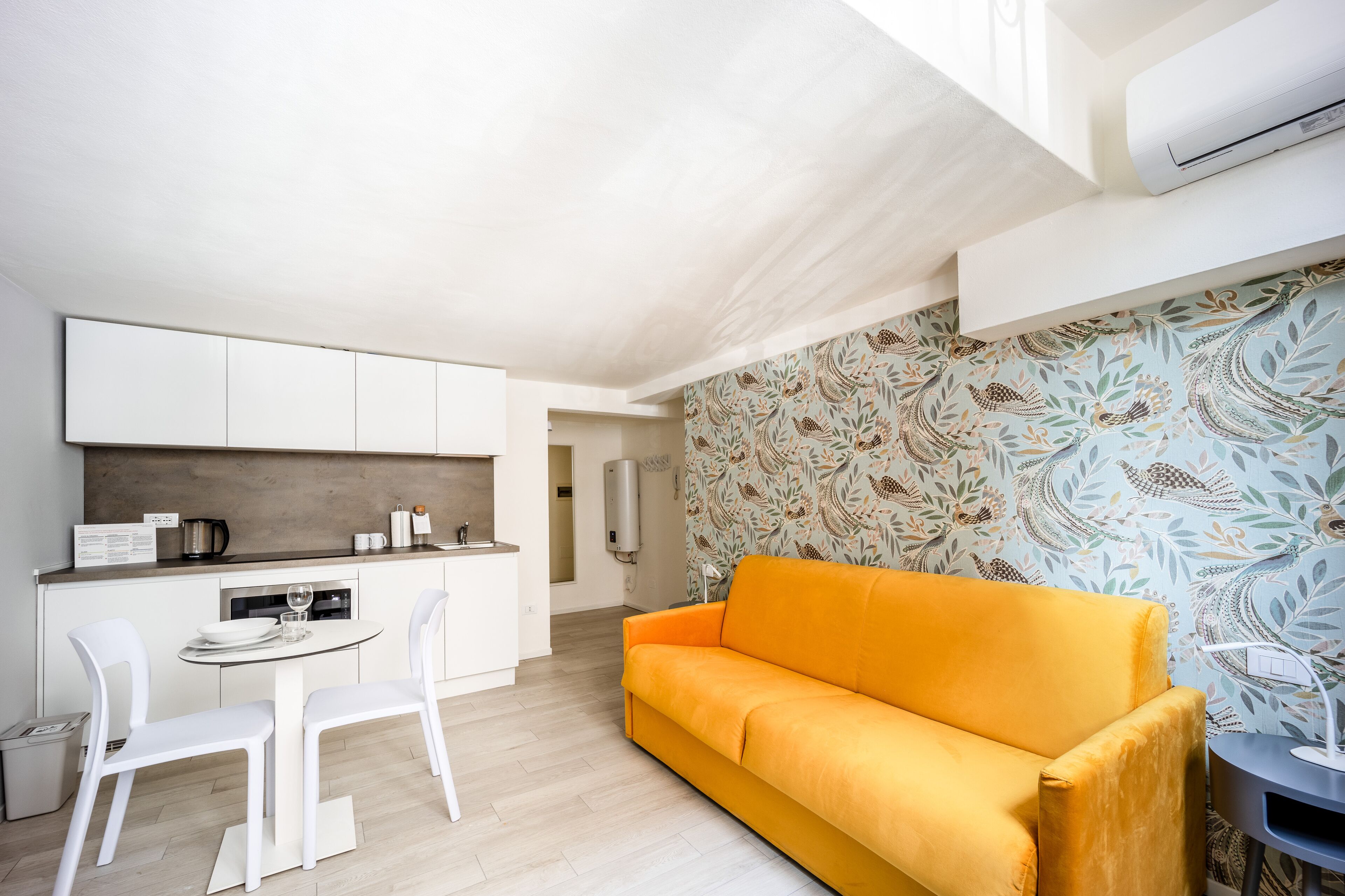 Una cocina moderna con armarios blancos, una mesa de comedor con sillas y un sofá naranja brillante.