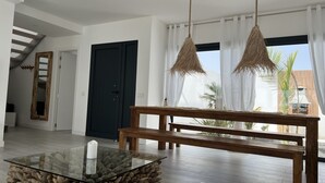 Un salon moderne avec une table basse en verre, un banc en bois et une porte sombre.