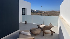 Un balcon extérieur moderne au design minimaliste, comprenant un espace détente avec un canapé et deux fauteuils en bois, une petite table et un panier en osier.