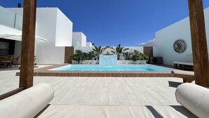 Un espace piscine agrémenté d’une pergola en bois, de murs blancs et d’un ciel d’un bleu limpide.