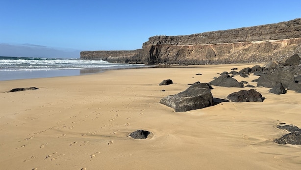 Une plage avec de gros rochers et une falaise en arrière-plan.