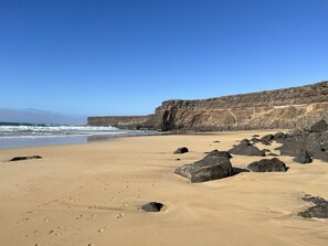 A beach with large rocks and a cliff in the background.