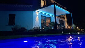 Una casa moderna con piscina, que cuenta con un patio cubierto y una entrada bien iluminada.