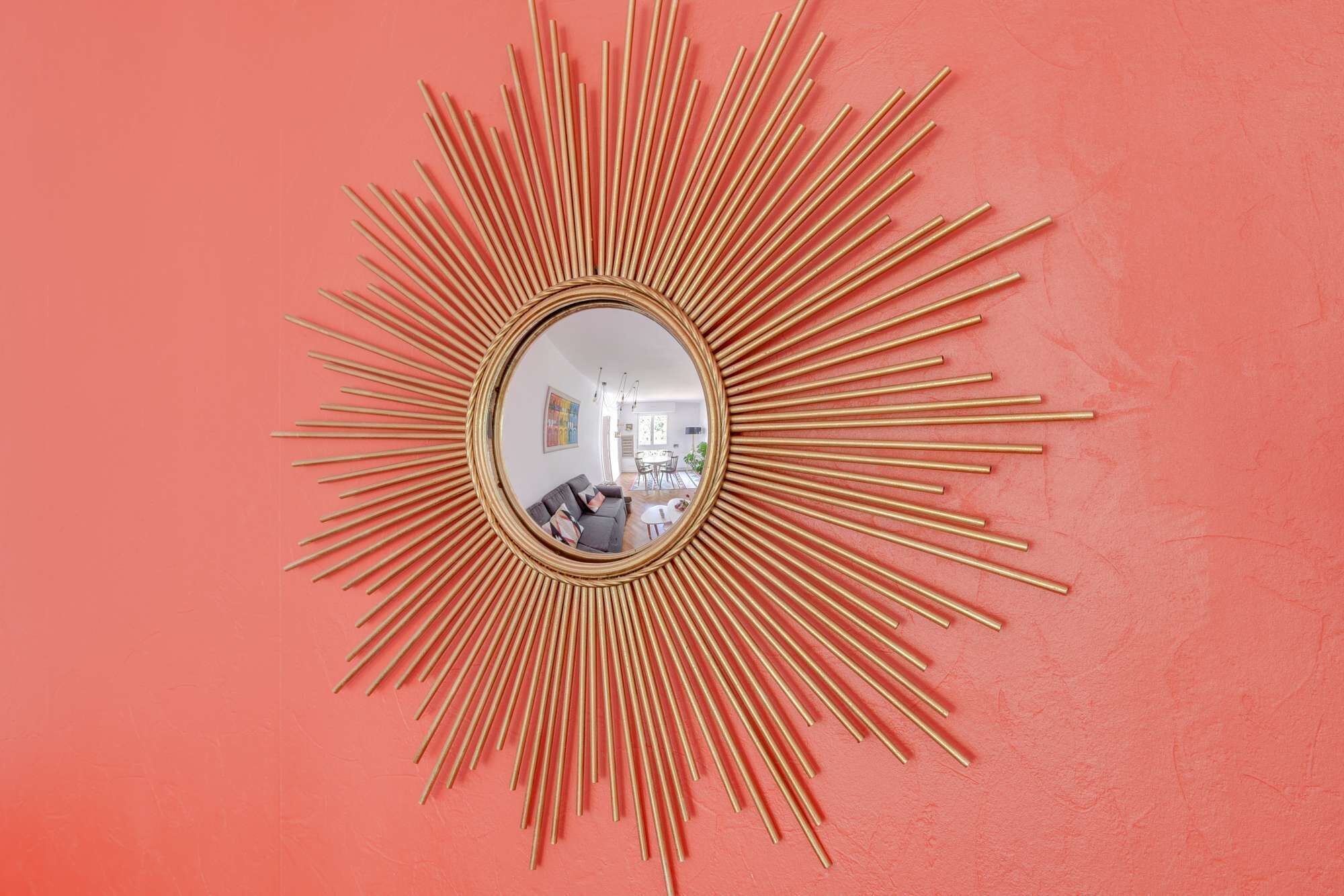Een spiegel met zonnestralen en een ronde lijst aan een roze muur.