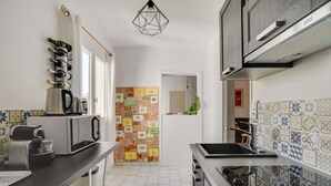 Une cuisine moderne équipée d’un four à micro-ondes, d’un grille-pain et d’une bouilloire sur le plan de travail. On y trouve également un meuble avec un four encastré et un évier. La cuisine est dotée d’un dosseret carrelé et d’un luminaire suspendu.