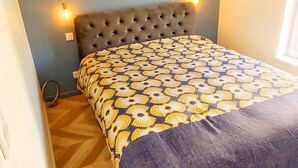 Un dormitori amb un capçal de llit amb vombros, un estovat estampat i un terra de fusta amb motius de petons.