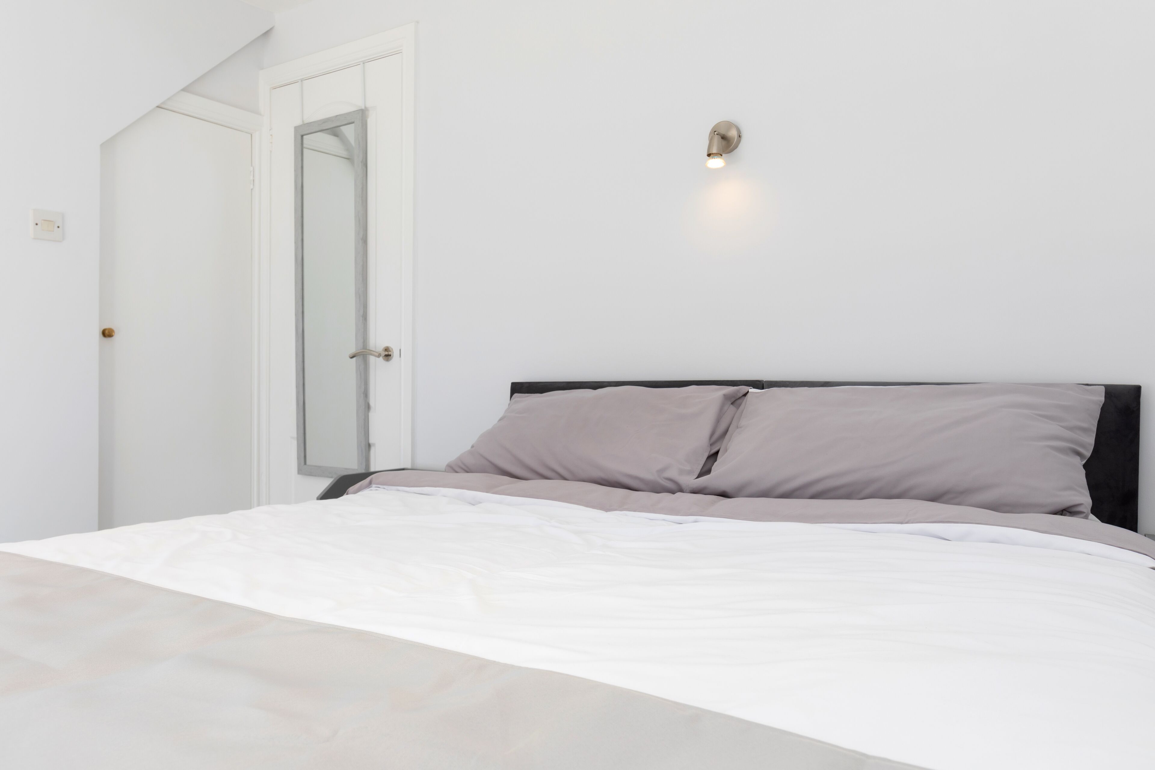 A bedroom with a bed, a door, and a wall-mounted light fixture.