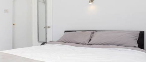 A bedroom with a bed, a door, and a wall-mounted light fixture.