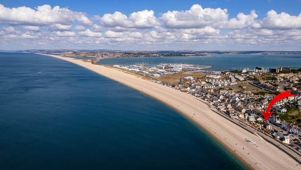 An aerial view of a coastal town with a long sandy beach, a marina, and residential buildings along the shore. - Cozy Cove Chapel (Portland)