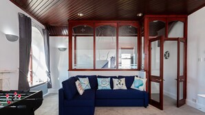A room with a foosball table, a blue sofa with decorative pillows, and a large window with a view of the outside. - Cozy Cove Chapel (Portland)
