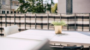 A balcony with a checkered cushion, a white table, and a potted plant. - Luga Homes - Gewandhaus (Leipzig)