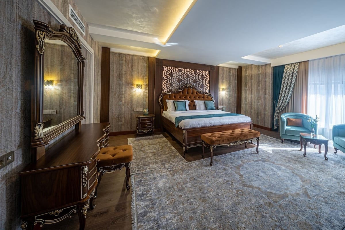 A spacious bedroom with a large bed, a dresser, a chair, and a mirror.
