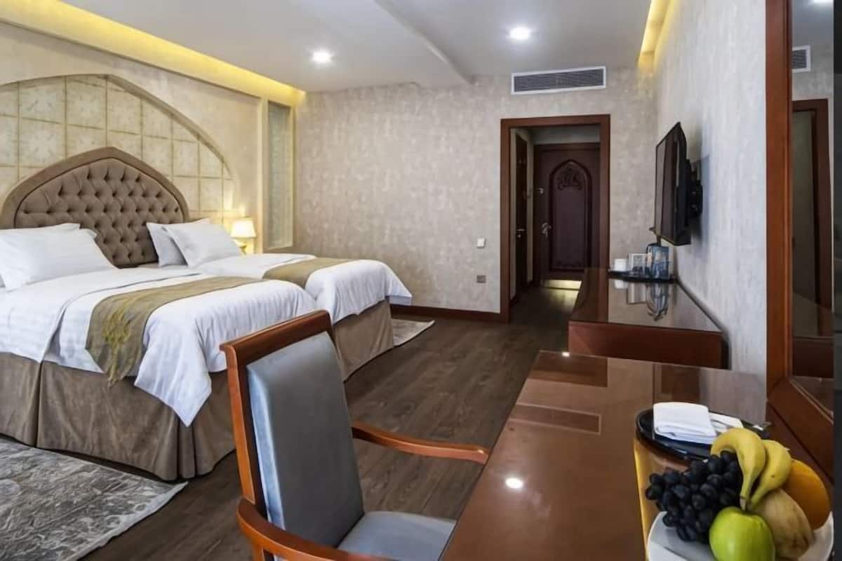 A hotel room with two beds, a wooden desk, a chair, a television, and a fruit bowl.
