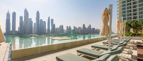 Piscina no terraço com espreguiçadeiras e guarda-sóis, com vista para o horizonte urbano.