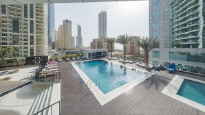 A rooftop pool with lounge chairs and a view of surrounding high-rise buildings.