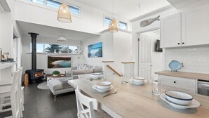 A modern kitchen with a central island, white cabinetry, and a large window overlooking a scenic landscape. - By the Bay on Duncan by Experience Jervis Bay (Vincentia)