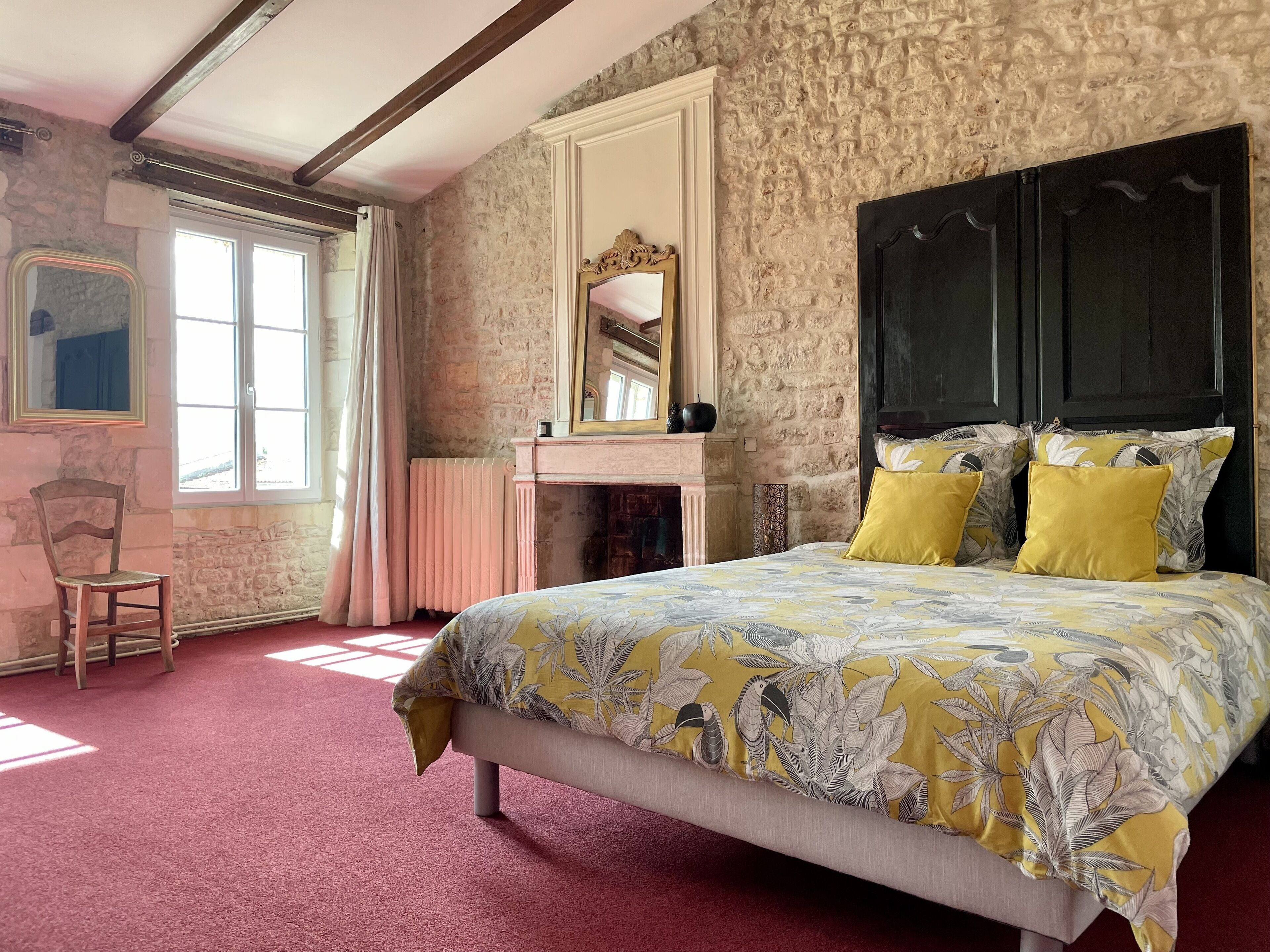 A bedroom with a bed, a chair, a dresser, a mirror, and a stone wall.