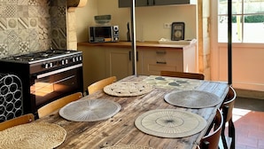 Una cocina rústica con pared de piedra, una mesa de madera con individuales tejidos, una estufa a gas y una planta colgante.
