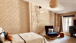 Un dormitorio con cama, una silla, una mesita, televisión y ventana.