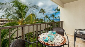 Een balkon met een ronde tafel, stoelen en uitzicht op palmbomen en een strand.