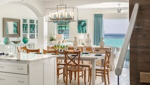 Een ruime eethoek met een groot eiland en meerdere stoelen, een hanglamp en uitzicht op de oceaan.