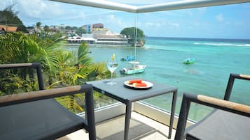 Un balcon avec une table, des chaises et une vue sur l’océan, où l’on peut apercevoir des bateaux.
