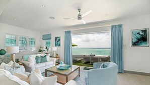 Een ruime woonkamer met een groot raam met uitzicht op de oceaan, een plafondventilator en een zithoek met zicht.