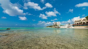 Een strand met helder turquoise water, een rotsachtige kustlijn en gebouwen met balkons met uitzicht op zee.