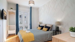 A bedroom with a bed, bedside lamps, a bedside table, a wardrobe, and a television on the wall. - Stylish Comfortable Flat w/ Balcony by HostWise (Porto)