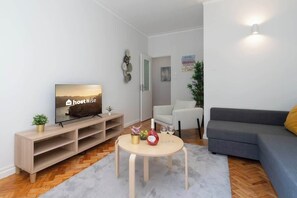 Una sala moderna con televisor, una mesa redonda, un sofá y una puerta que da a otra habitación.