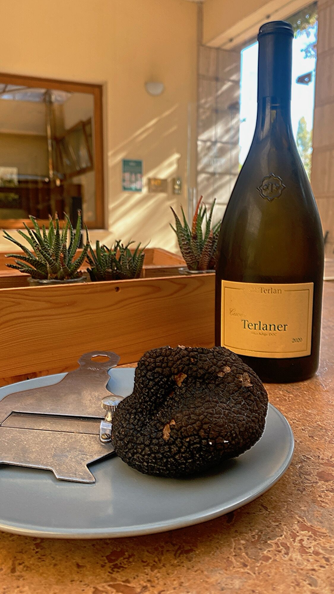 Una botella de vino Terlan, una trufa de chocolate negro y una escultura de metal sobre un plato.