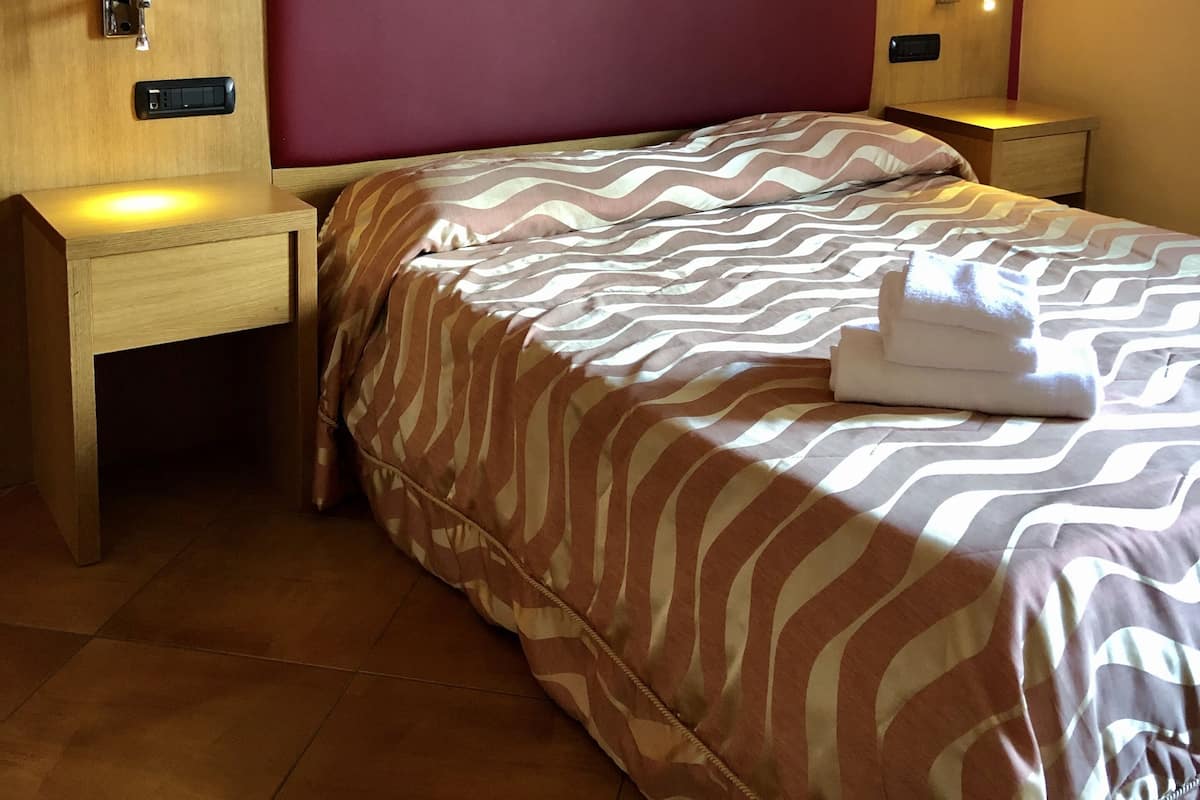 A hotel room with a bed, two bedside tables, and two wall-mounted lamps.