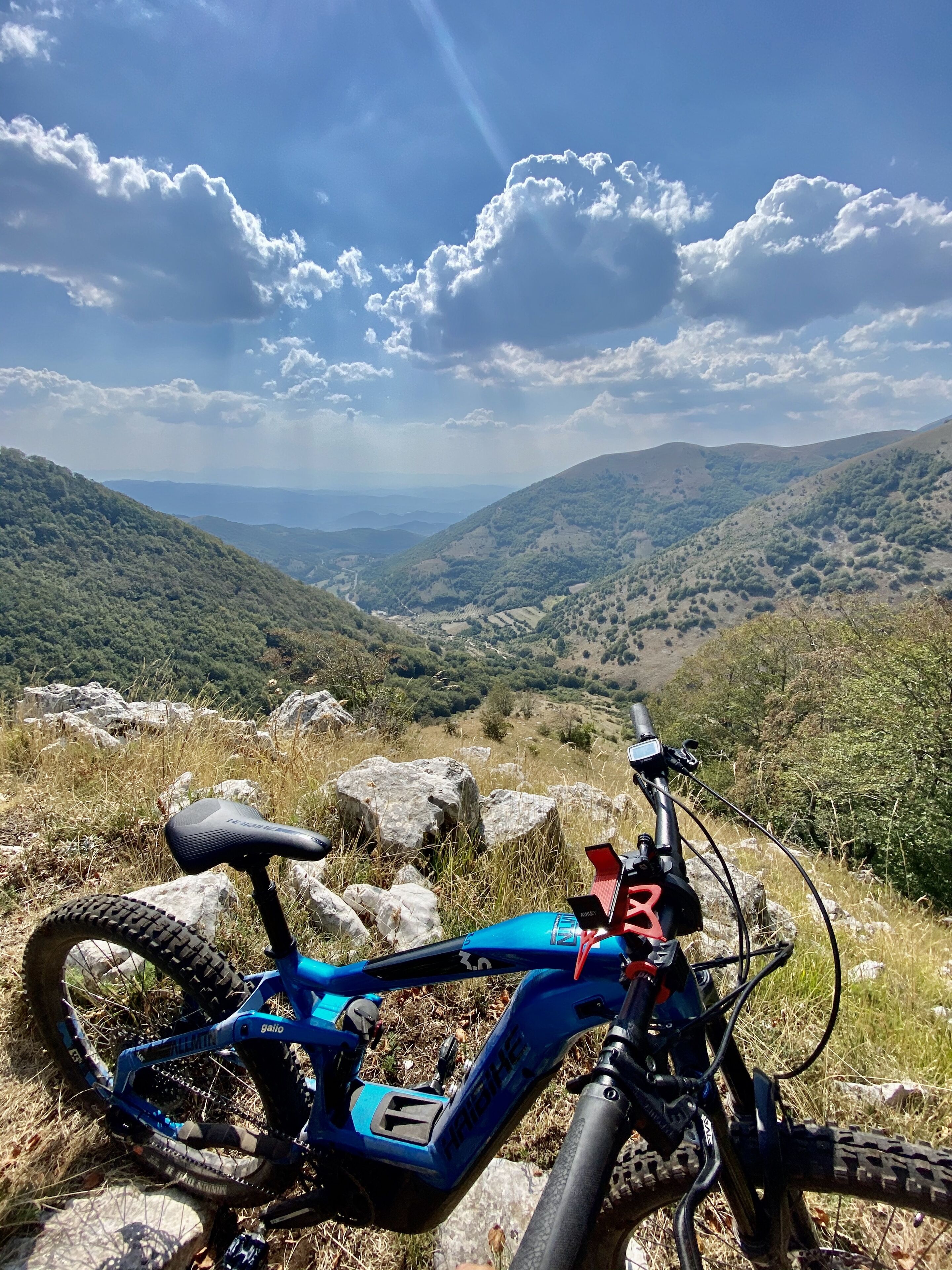 A mountain bike parked on rocky terrain with a scenic view of green hills and a clear sky.