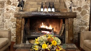 A stone fireplace with a fire, a glass table with a floral arrangement, and four bottles on the mantel. - Albergo Mingone (Arpino)