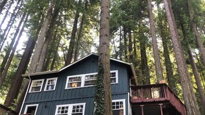 A two-story cabin with a balcony, surrounded by tall trees. - Hillside Retreat in the Redwoods w/ Hot Tub (Guerneville)