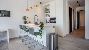 A modern kitchen with a central island, bar stools, pendant lighting, and a trash bin. - Blue Bay - The Reef (Sint Michiel)
