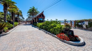 A paved pathway leading to a building with a wooden gate, surrounded by lush greenery and red flowers. - 35581 Beach Road: 4  BR, 4  BA House in Dana Point, Sleeps 8 (Dana Point)
