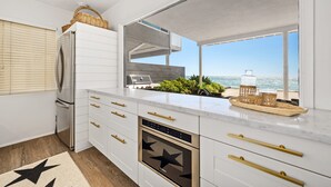 A modern kitchen with white cabinetry, gold handles, a built-in oven, and a view of the ocean. - 35581 Beach Road: 4  BR, 4  BA House in Dana Point, Sleeps 8 (Dana Point)