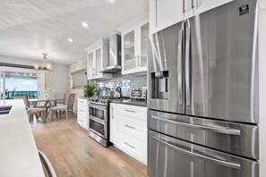 Cozinha moderna com eletrodomésticos de aço inoxidável, armários brancos e vista para o exterior.
